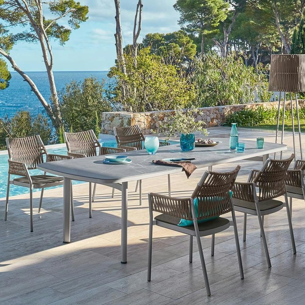 elegant contours: shifting hues of anodized aluminum frames capture the sun in the 110" ceramic dining table and grey-brown armchairs