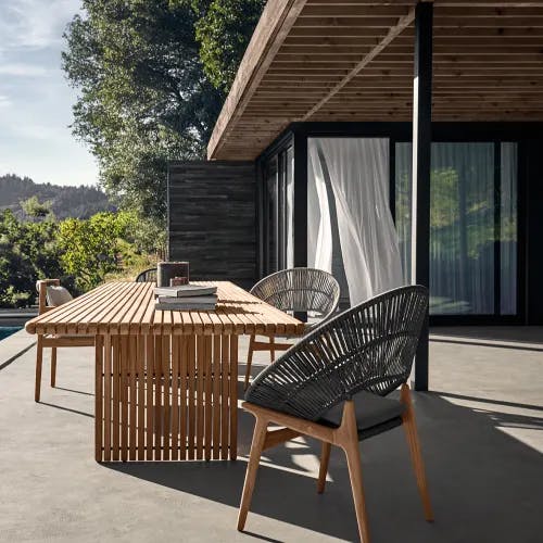 Gloster Bora + Deck Dining Set of three chairs and one outdoor dining table in the backyard in front of a pool.